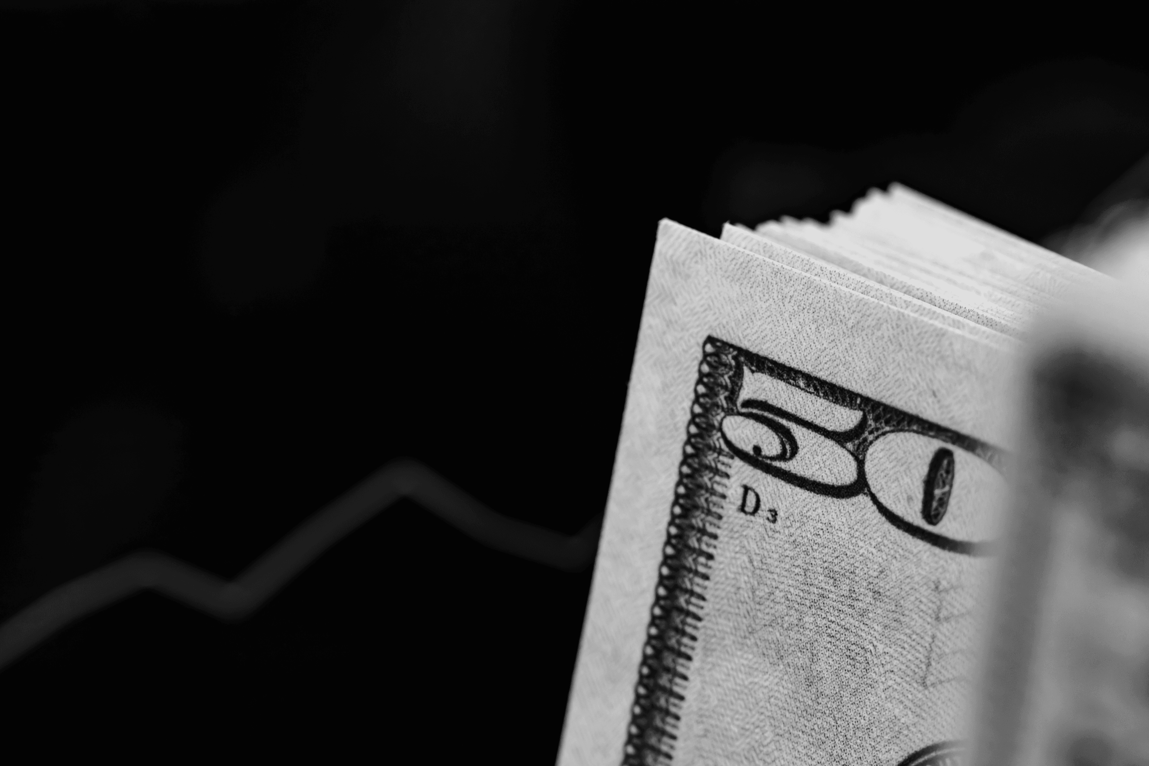 A close-up captures a stack of money against a dark background, featuring a blurred blue financial growth chart.