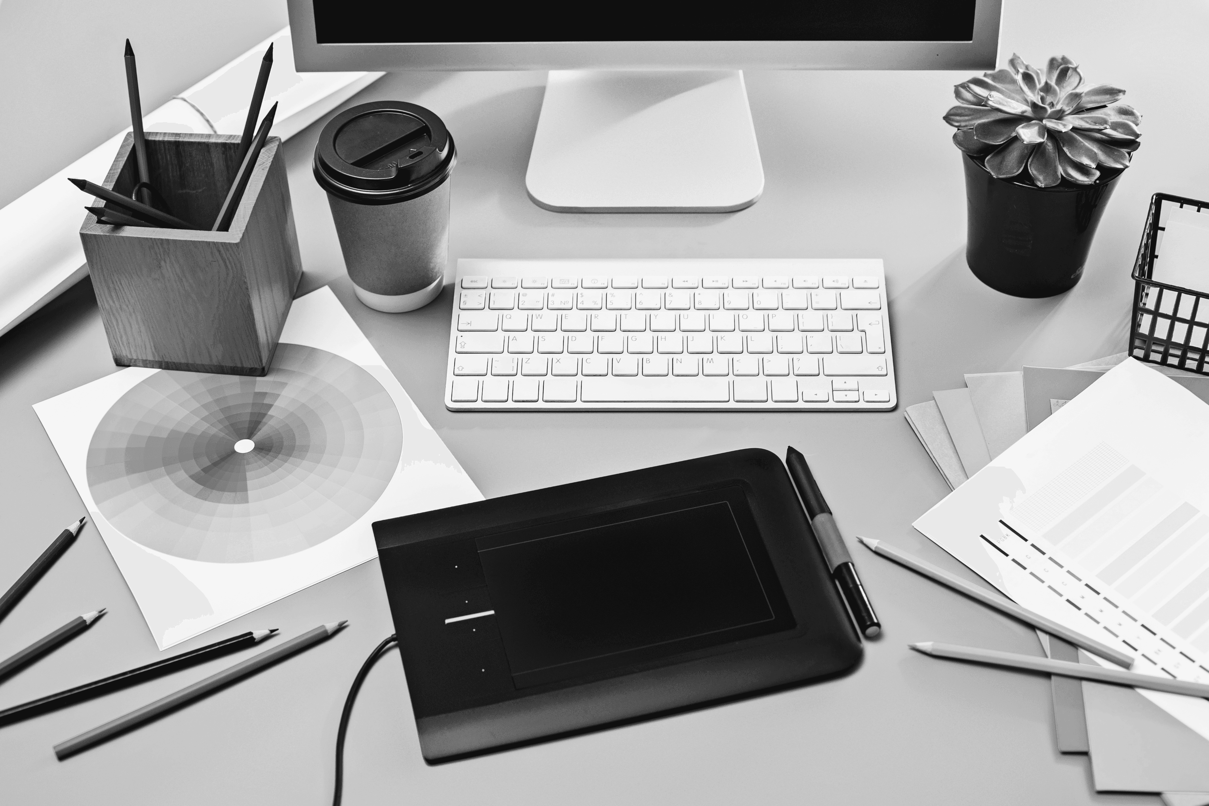 An eye-level medium shot presents a desktop computer alongside an arrangement of everyday objects on a wooden desk.